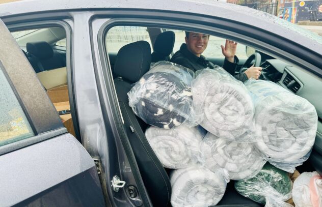 Someone waving in a car loaded with donated items like blankets.