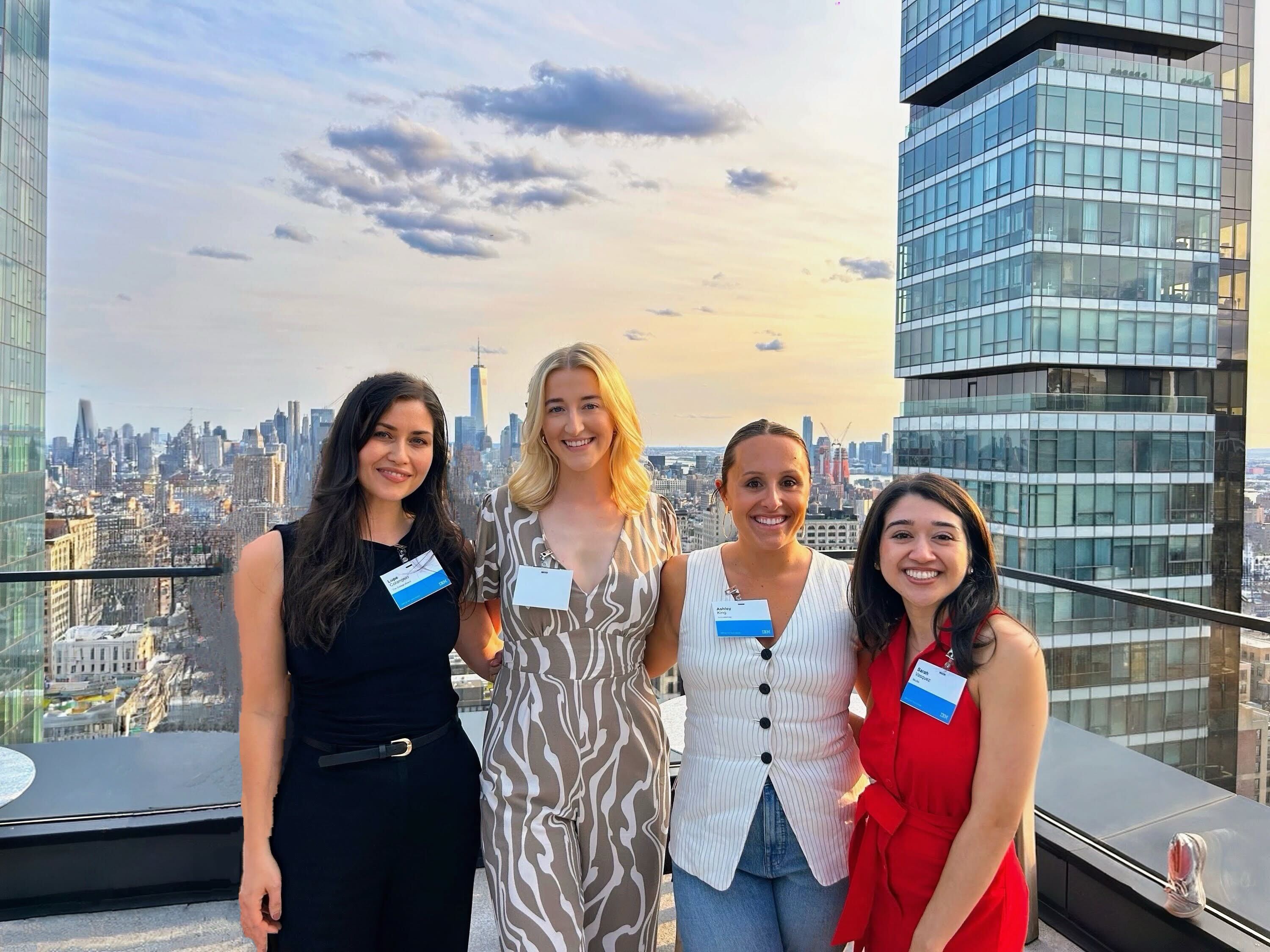 Four women smile for a photo on a rooftop during NYC Tech Week, with the city skyline and sunset in the background.